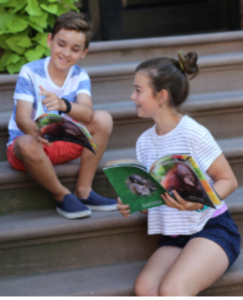 Henry Kurzawa and Maeve Igoe, PS 107 5th graders, celebrate the successful rescue of orphaned orangutan Budi while reading their newly published book. Photo courtesy of Ericka Novotny. 